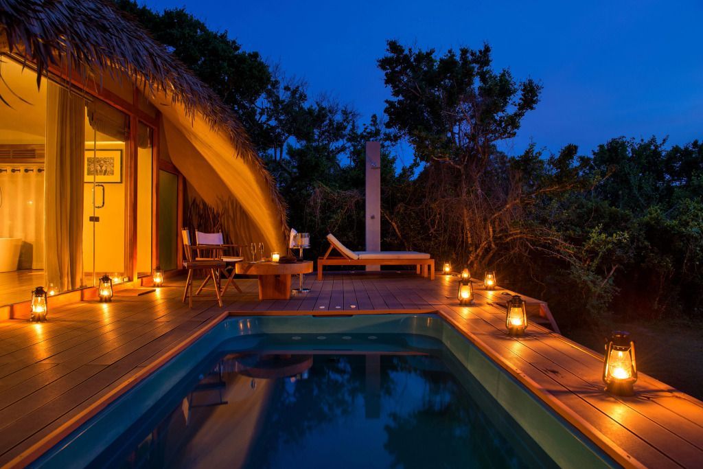 Beleuchteter Pool auf Terrasse einer Villa bei Nacht.