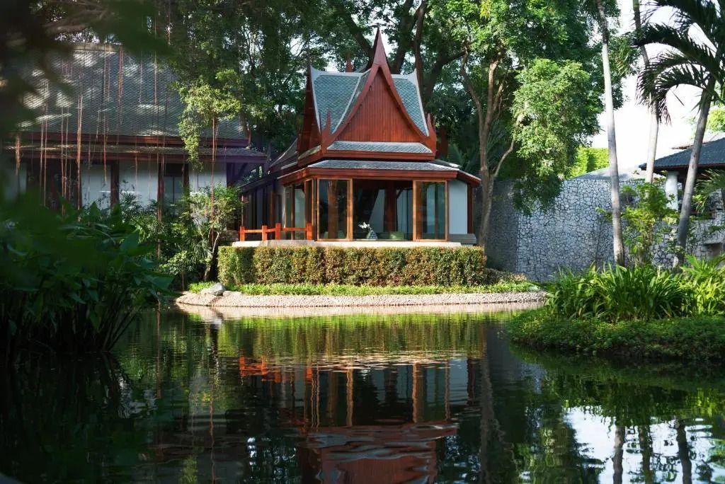 Traditionelle Villa mit spitzem Dach am Rand eines Teiches, von Bäumen umgeben