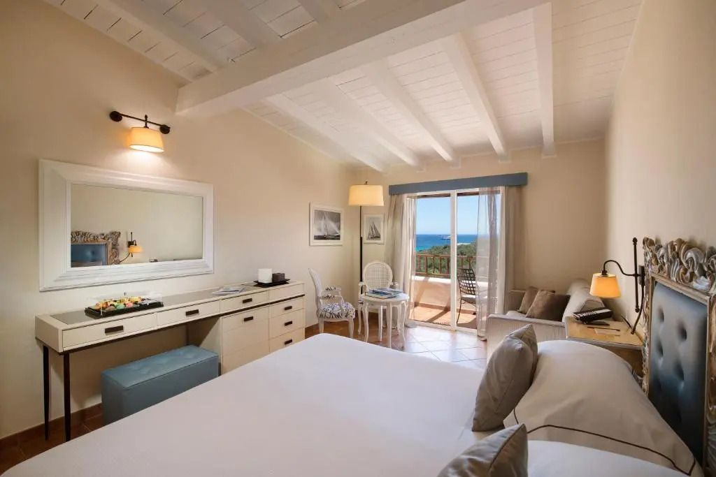 Elegantes Hotelzimmer mit Doppelbett, hellem Dekor und Meerblick vom Balkon.