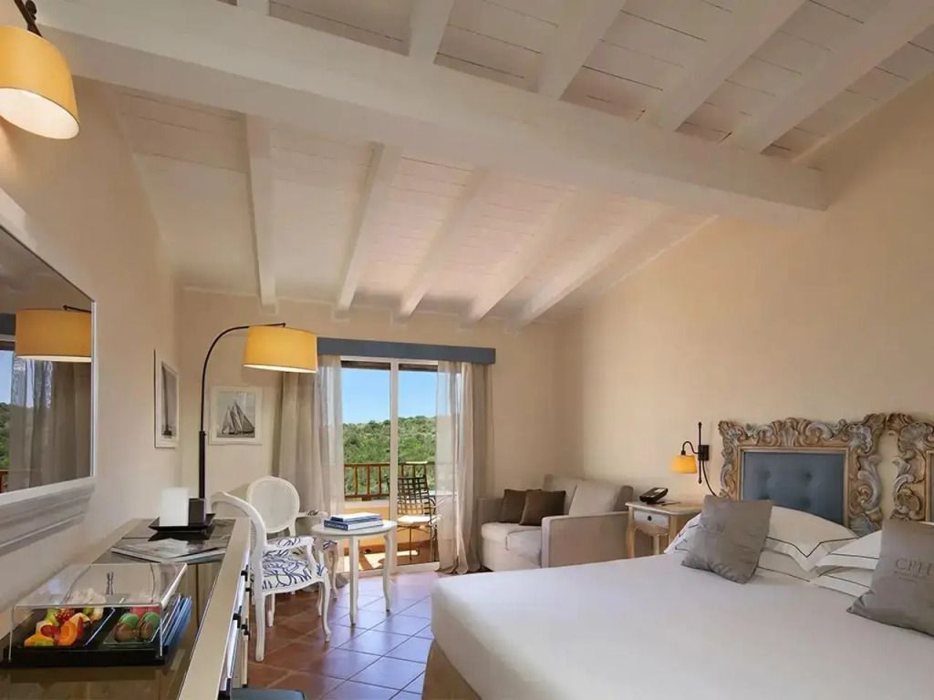 Helles und stilvolles Doppelzimmer mit Balkon im Pevero Hotel und Blick auf die Natur.