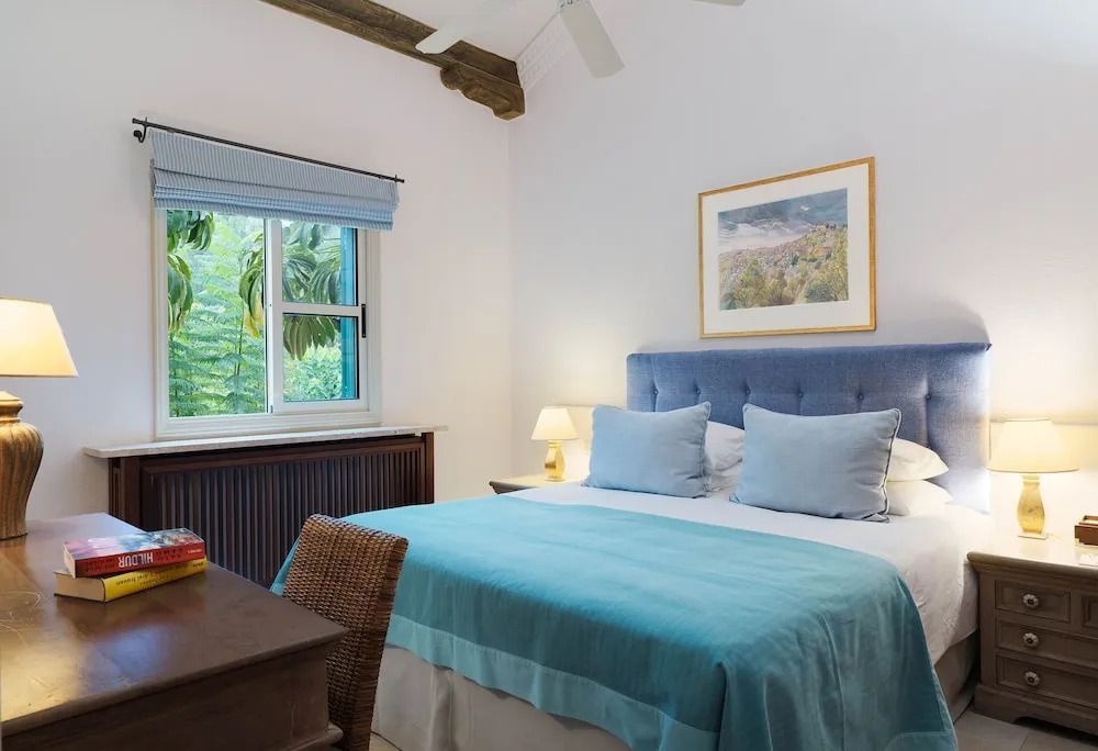 Schlafzimmer mit großem Bett, blauer Bettwäsche und Fenster mit Gartenblick.