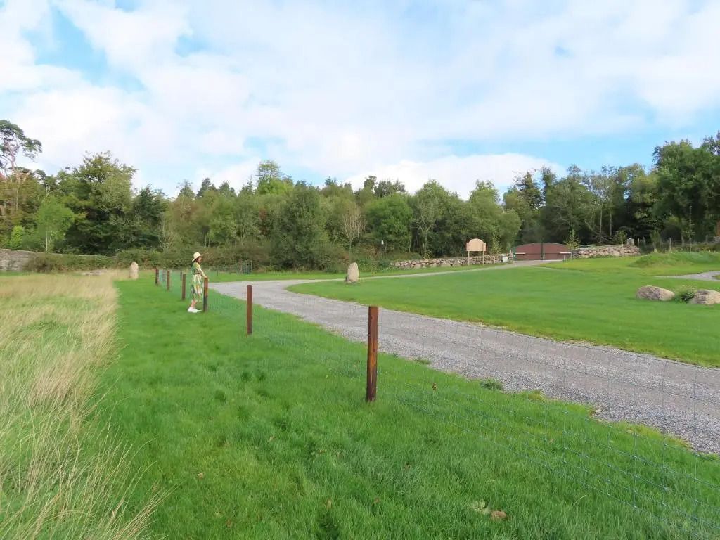 Grüne Landschaft mit Spazierweg und bewaldetem Hintergrund