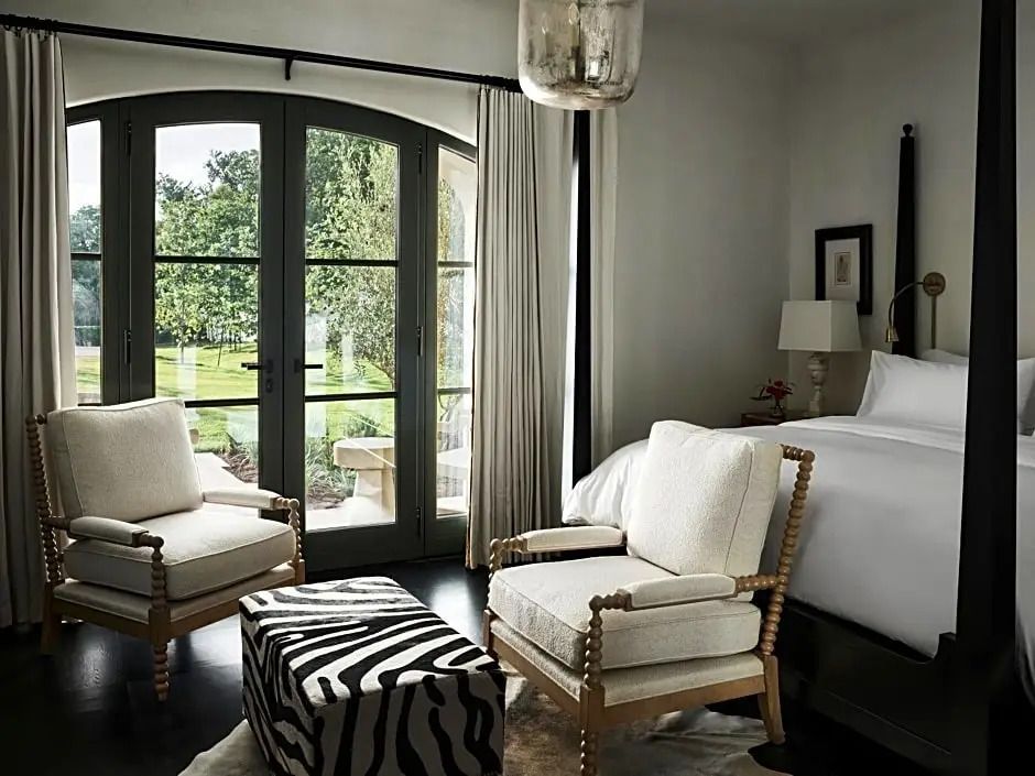 Elegantes Hotelzimmer mit Doppelbett, Sesseln und Blick auf einen Garten