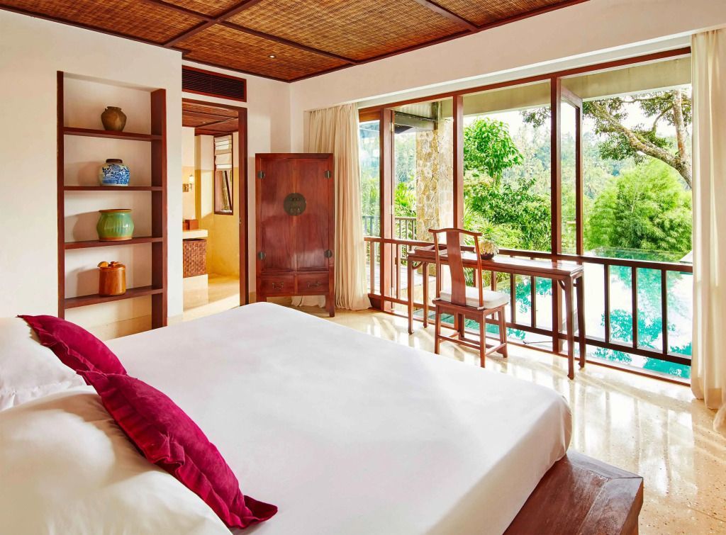 Helles Schlafzimmer mit großen Fenstern und Blick auf tropische Gärten im COMO Shambhala Estate.