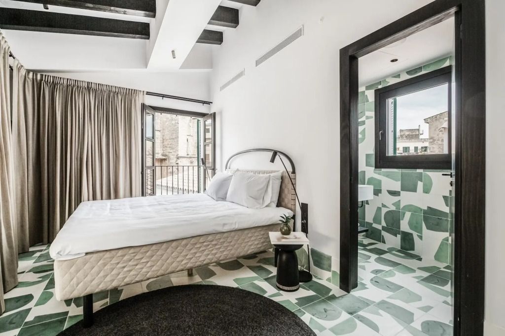 Helles Schlafzimmer mit Doppelbett und stilvollem Badezimmer mit grün-weißem Mosaik.