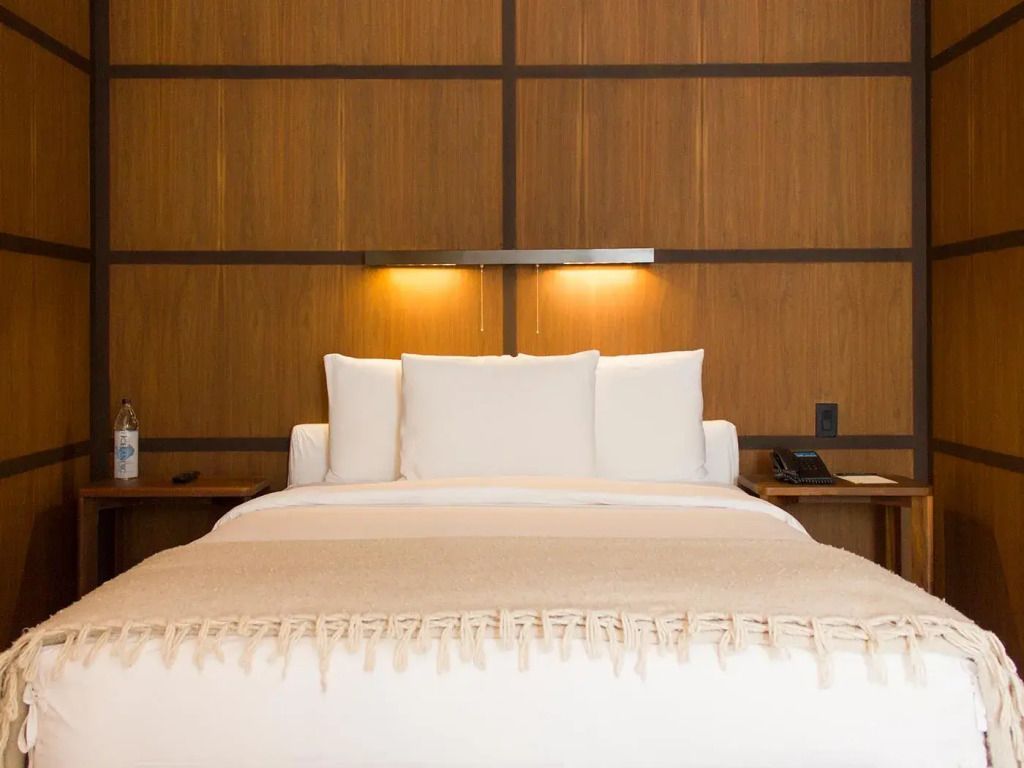 Gemütliches Doppelbett mit Holzwand und sanfter Beleuchtung im Condesa DF Hotelzimmer