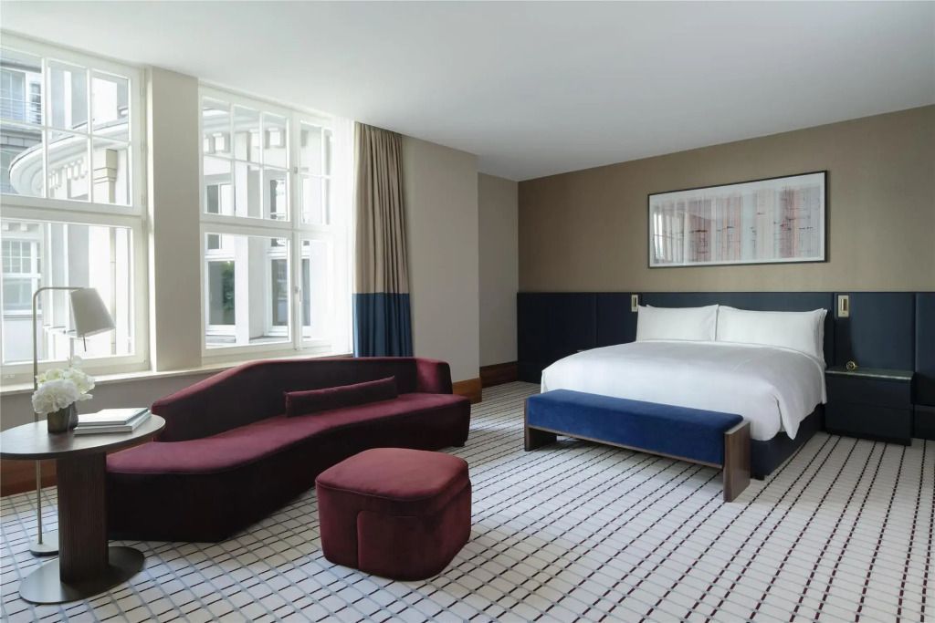 Geräumiges Zimmer mit modernem Sofa und großem Doppelbett vor hellen Fenstern.
