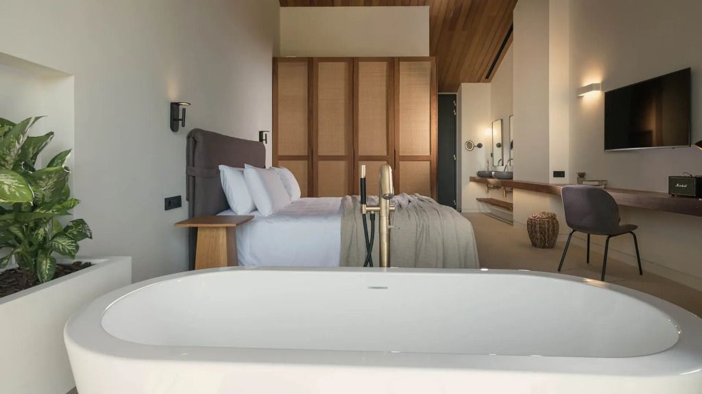 Elegantes Doppelbett vor Holzwand in Junior-Suite mit moderner Badewanne im Vordergrund