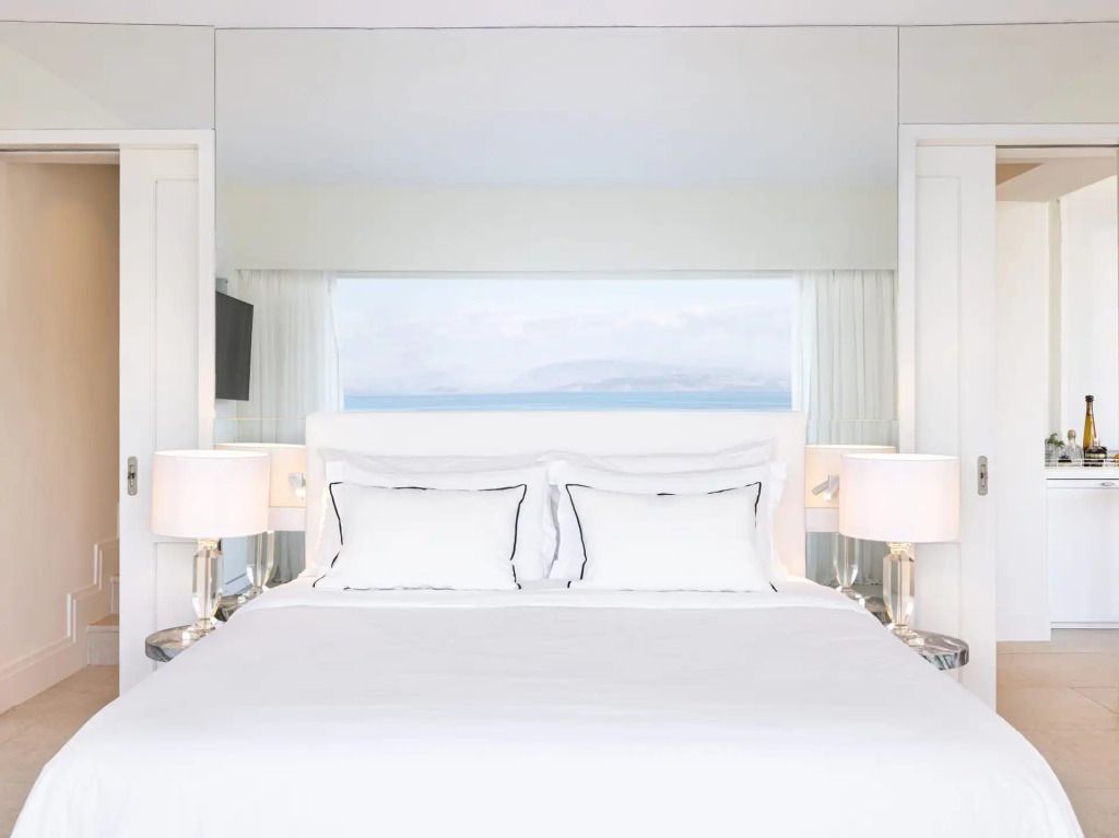 Helles Schlafzimmer mit großem Bett und Blick auf das Meer durch ein Fenster.