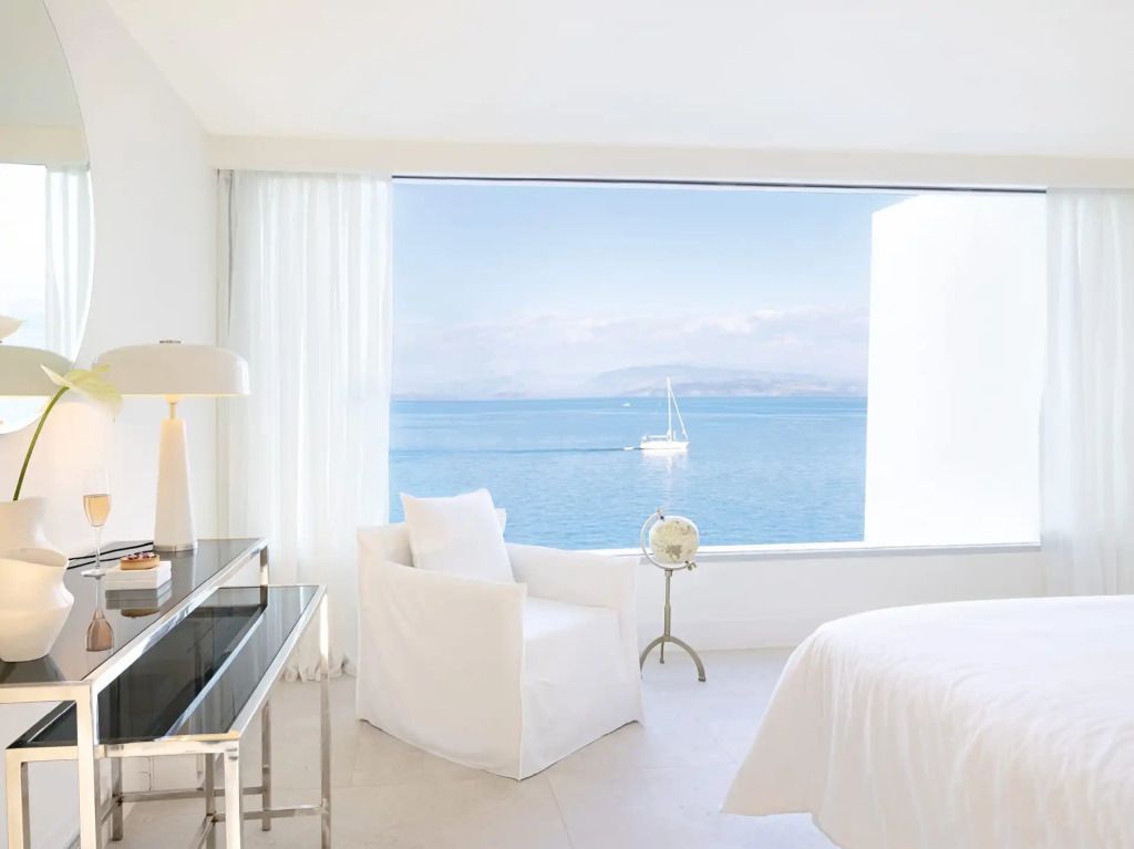 Zimmer mit großem Fenster und Blick auf das offene Meer mit Segelboot