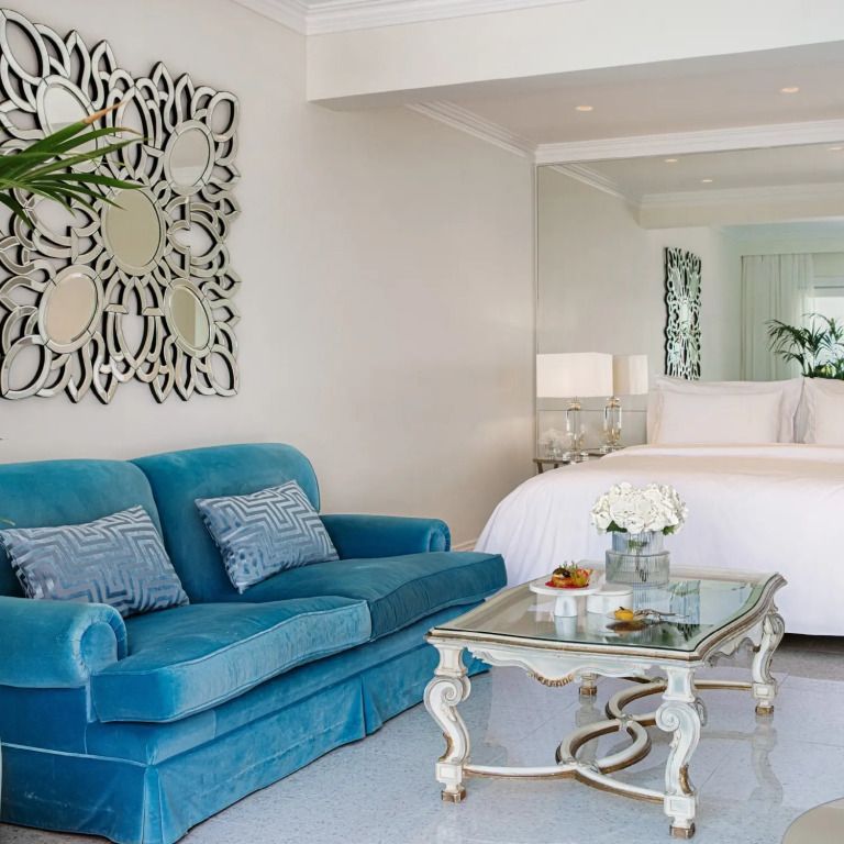 Offene Suite mit blauer Couch, Glas-Couchtisch und elegantem Bett.