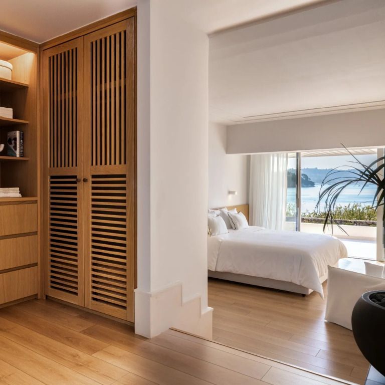 Helles Schlafzimmer mit Holzboden und Meerblick durch große Fenster.