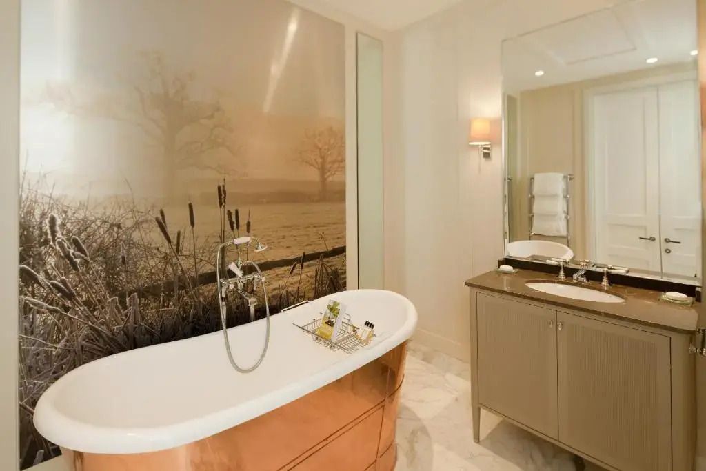 Luxuriöses Badezimmer mit freistehender Kupferbadewanne und Wandbild.