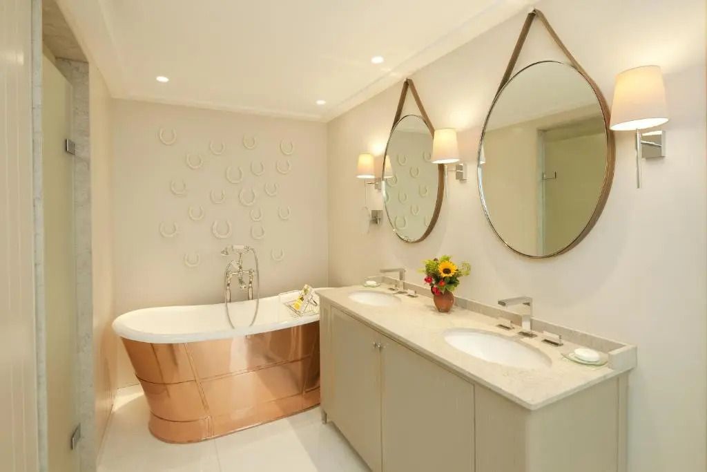 Badezimmer mit Kupferbadewanne, Doppelwaschbecken und dekorativen Spiegeln.