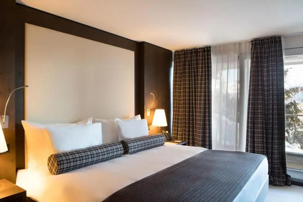 Elegantes Doppelzimmer mit großem Bett und bodentiefen Fenstern im Crans Ambassador Hotel.