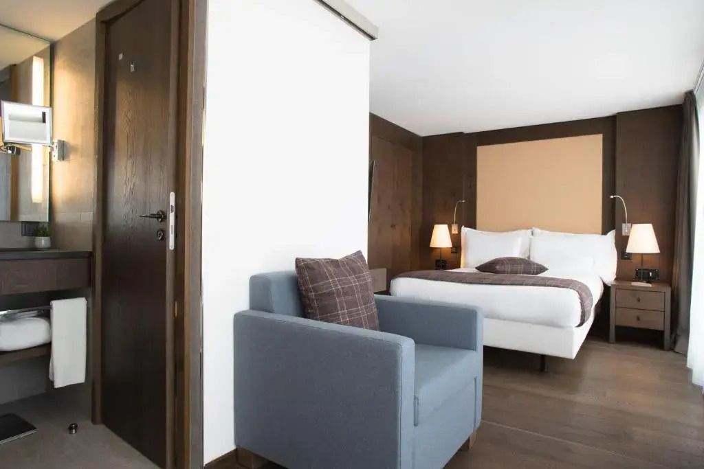 Modernes Einzelzimmer mit einem gemütlichen Sessel und Bett im Crans Ambassador Hotel