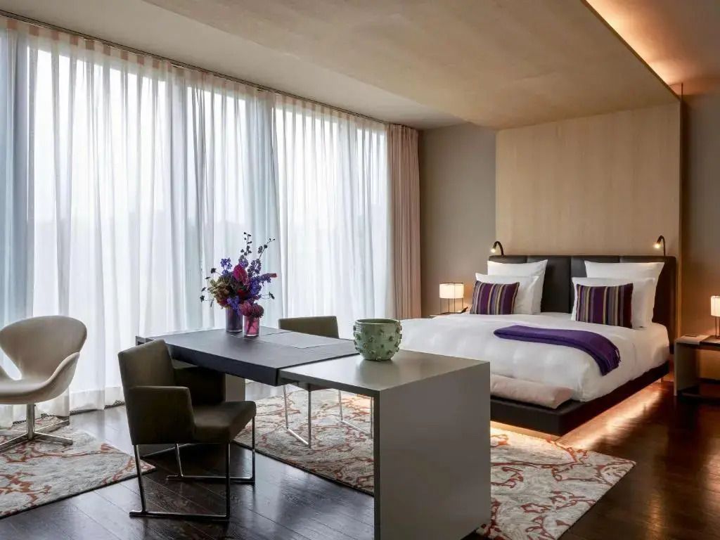 Helles Zimmer mit großem Fenster, Doppelbett und Blumenarrangement auf einem Schreibtisch