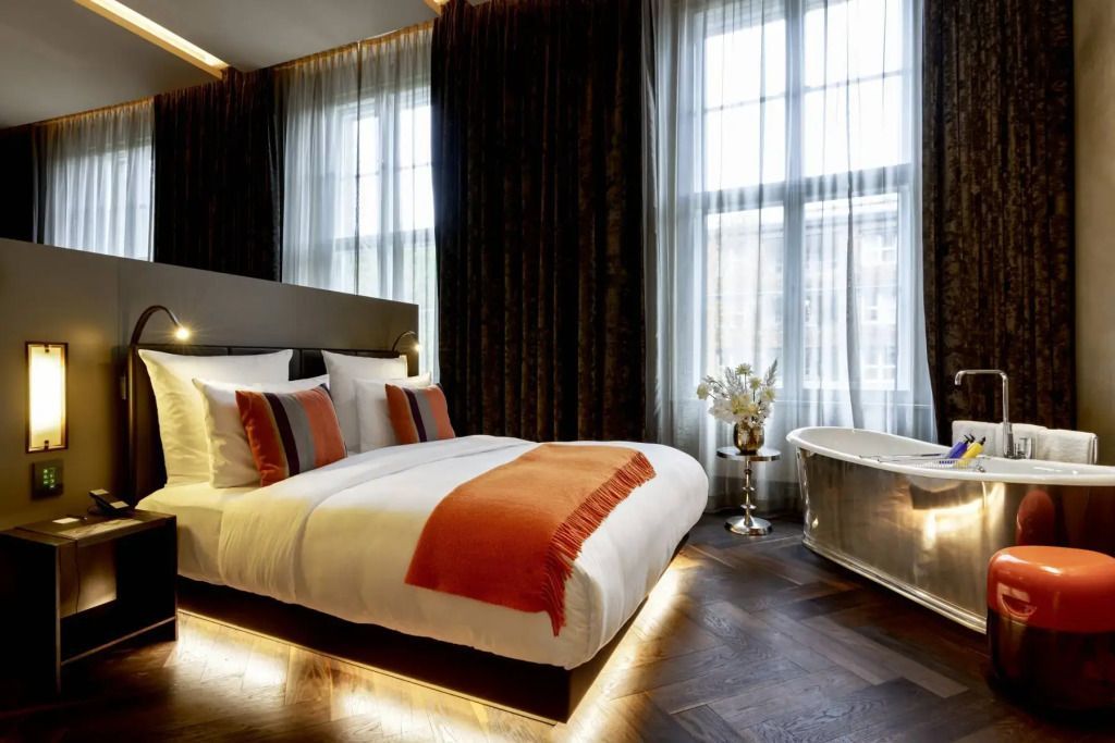 Modernes Schlafzimmer mit Doppelbett, orange Akzent und freistehender Badewanne