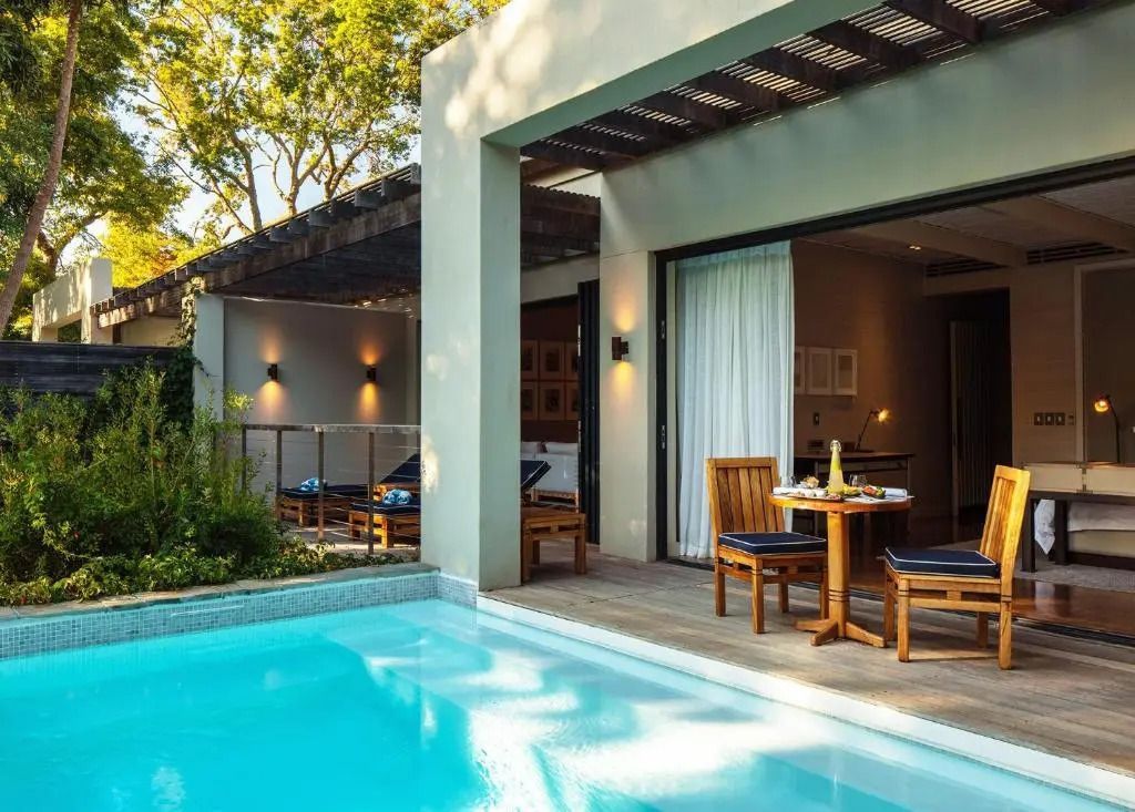 Pool und Terrassensitzbereich vor einer eleganten Villa im Grünen.