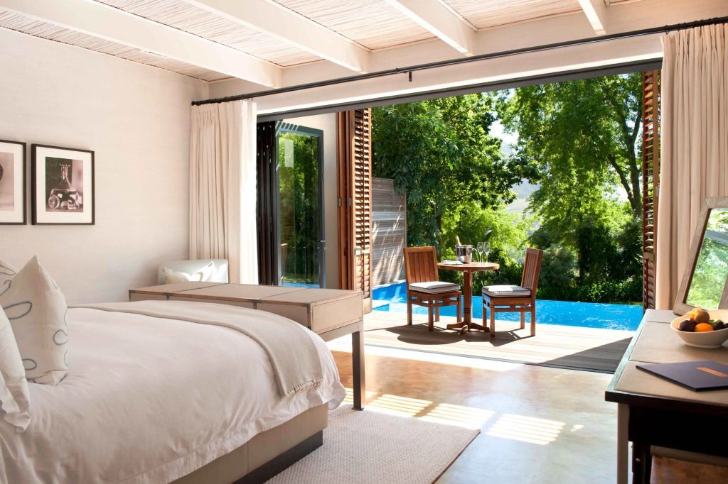Luxuszimmer mit offener Tür zur Terrasse mit Pool und Gartenblick