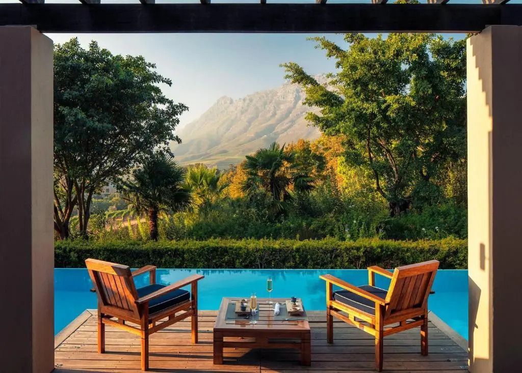 Zwei Stühle und Tisch auf einer Terrasse mit Blick auf Pool und Berge im Hintergrund