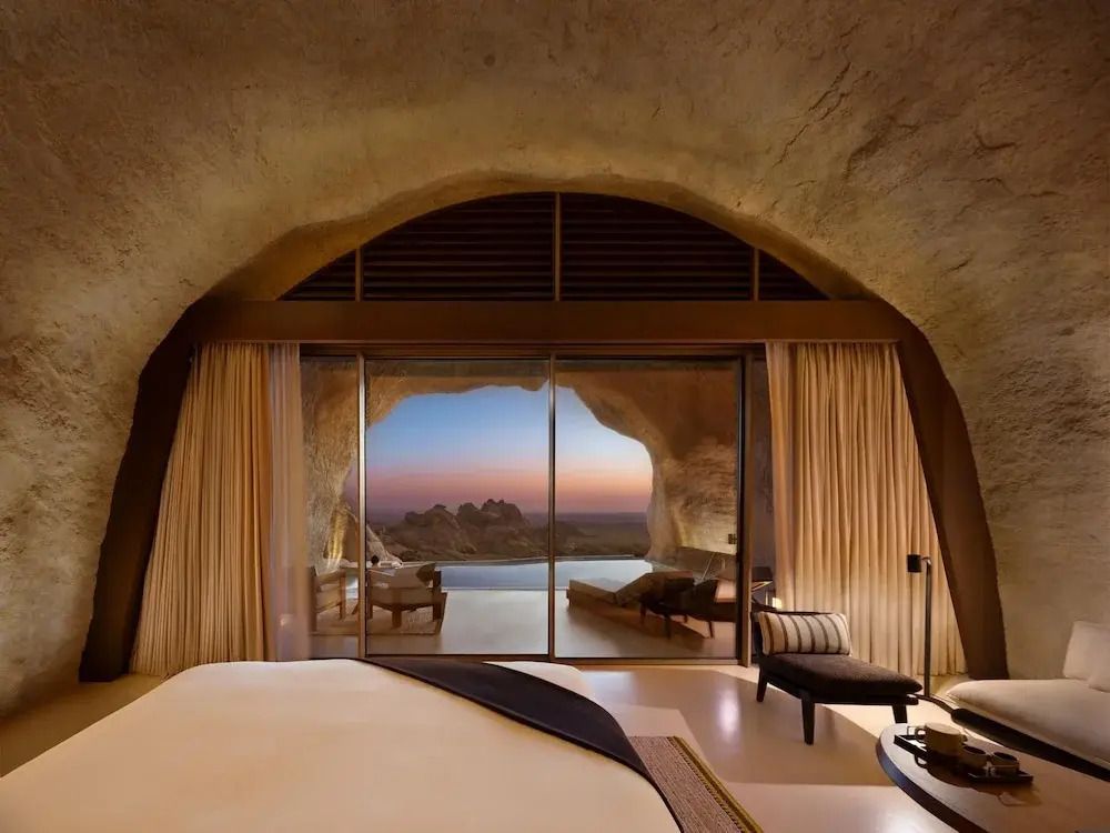 Suite mit großem Bett und Blick auf Balkon bei Sonnenuntergang durch Panoramafenster.