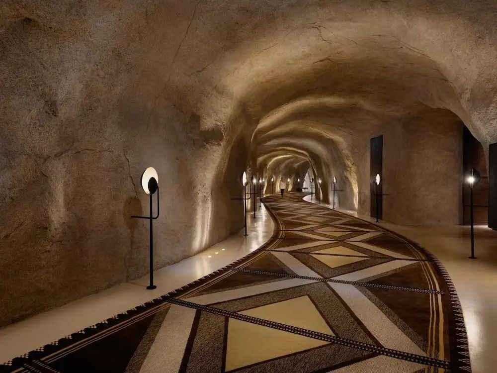Kunstvoll beleuchteter Hotelgang mit Natursteinwänden und geometrischen Mustern.