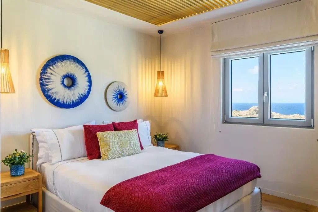 Helles Hotelzimmer mit Doppelbett und Meerblick durch ein Fenster