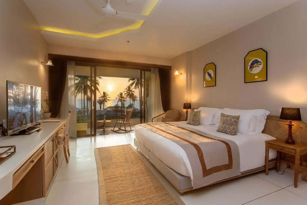 Geräumiges Hotelzimmer mit Doppelbett und Blick auf Sonnenuntergang über Palmen und Meer