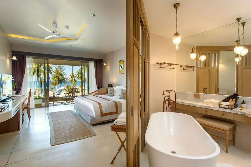 Offenes Hotelzimmer mit freistehender Badewanne, Bett und Balkon mit Meerblick