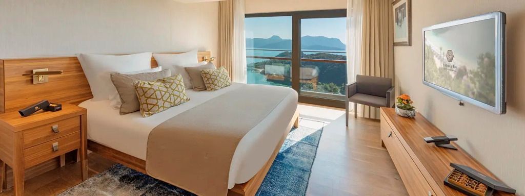 Doppelbett mit Meerblick in einem eleganten Hotelzimmer mit großen Fenstern