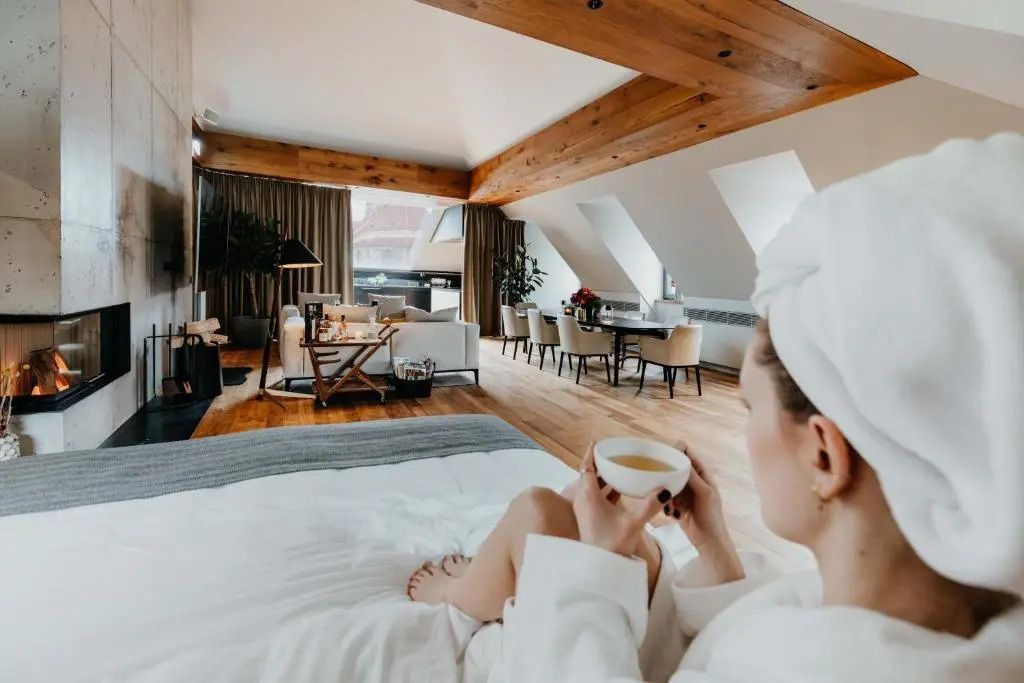Luxuriöses Penthouse-Zimmer mit Holzbalken, gemütlicher Sitzbereich und Frau mit Tasse