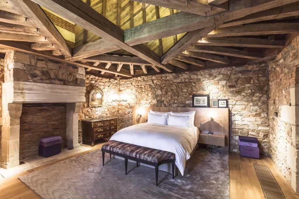 Rustikales Schlafzimmer mit Holzbalkendecke und Natursteinwänden im Domaine des Etangs.