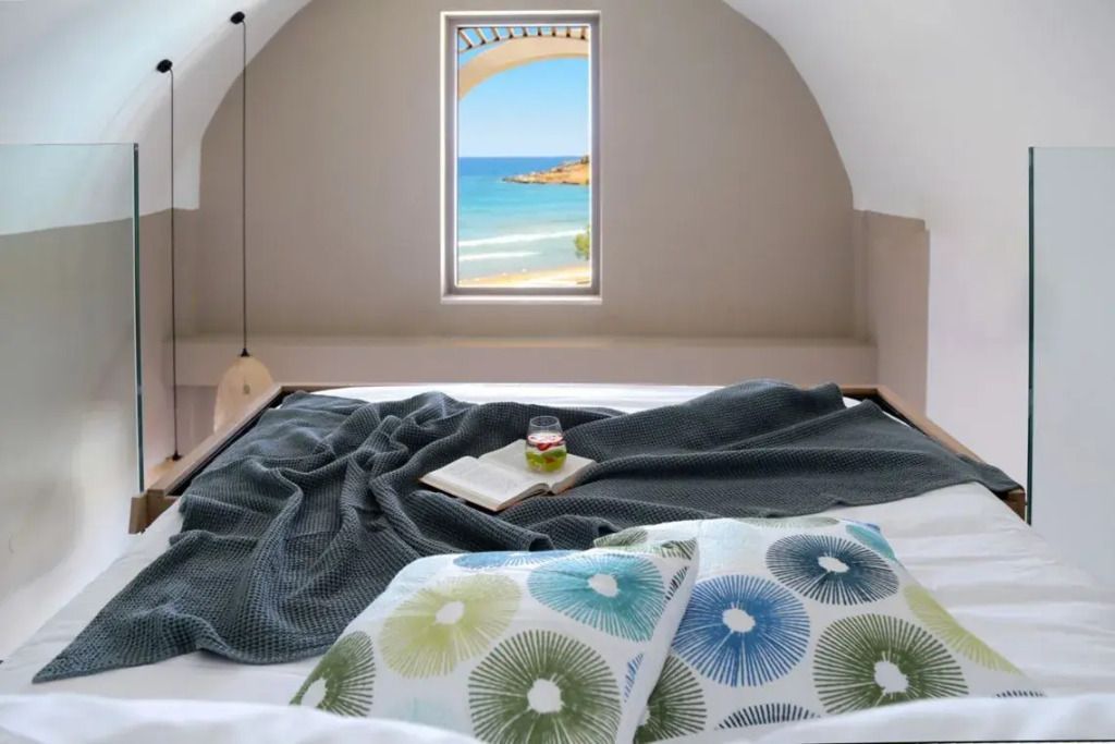 Blick vom Bett auf das Meer durch ein Fenster in einer Suite mit stilvollem Design.