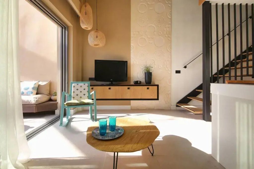 Gemütliche Sitzecke mit TV, Sessel und hängenden Lampen in einem sonnigen Loft.