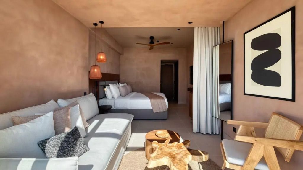 Helles Hotelzimmer mit Doppelbett, gemütlichem Sofa und Holztisch. Warme Beleuchtung.