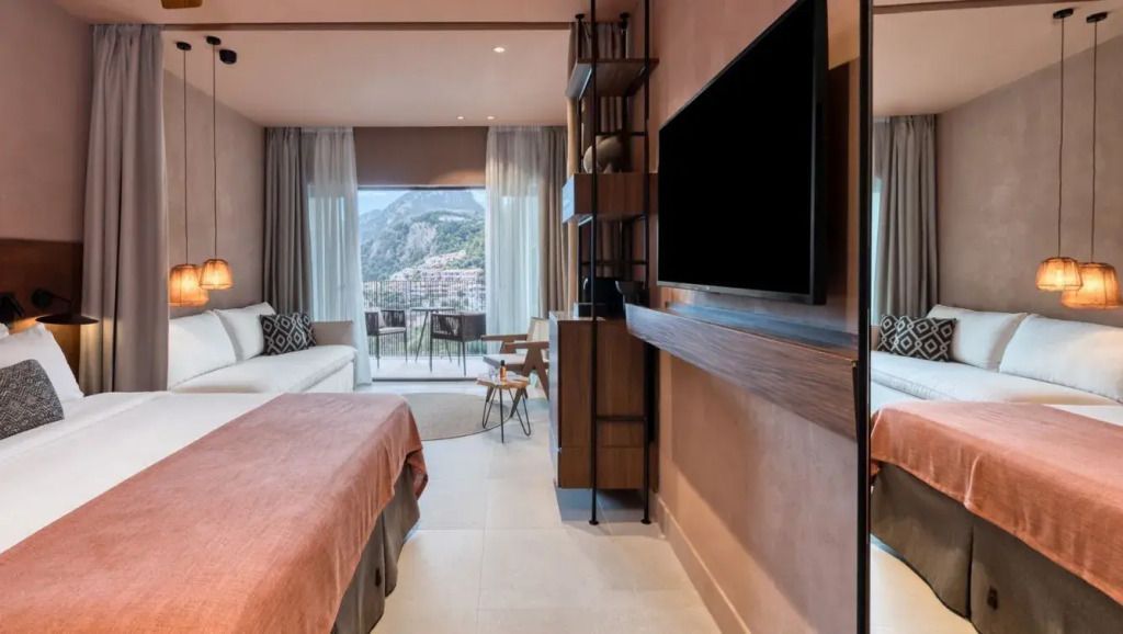 Zimmeransicht mit Doppelbett, großem Fernseher, Balkon mit Naturblick. Schmales Regal.