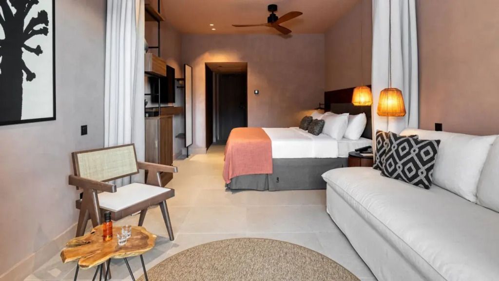 Helles Zimmer mit Doppelbett, Sofa, gemütlichem Sessel. Hölzerne Regale und moderne Lampen.