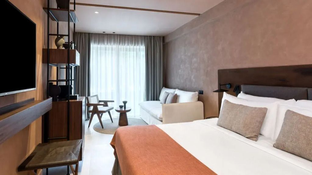 Helles Zimmer mit Balkonblick, kombiniert Bett und Sofa in warmen Farben.