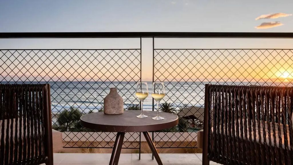 Balkon mit Tisch und zwei Weingläsern bei Sonnenuntergang über dem Meer