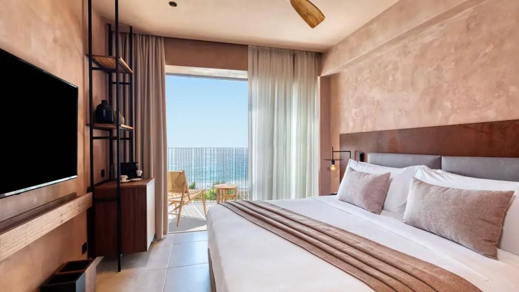 Helles Schlafzimmer mit Doppelbett, großem Fenster und Meerblick vom Balkon