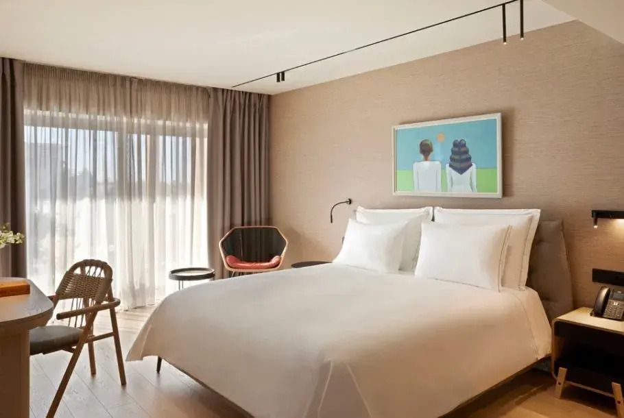 Elegantes Doppelbett in einer Suite mit modernem Kunstwerk an der Wand und Tageslicht.
