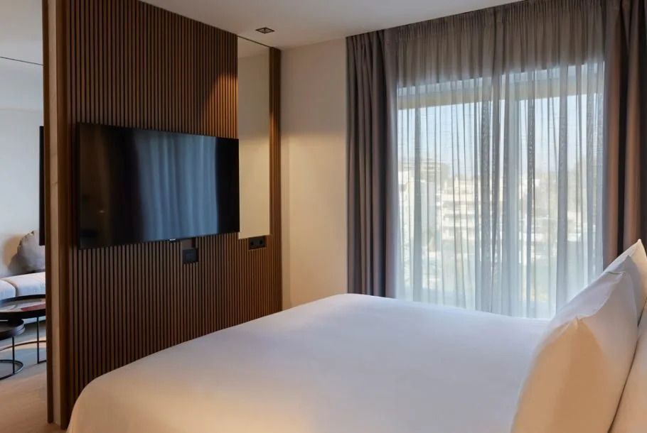 Große Fenster mit Vorhängen und Wand-TV im Schlafbereich der Suite.