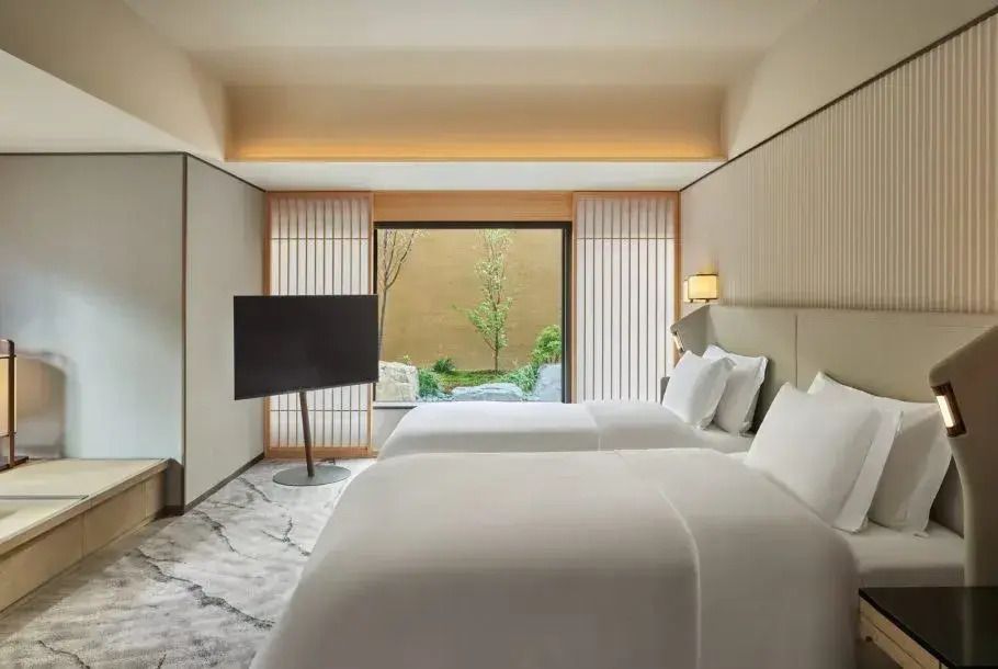 Geräumiges Hotelzimmer mit zwei Einzelbetten, modernem Dekor und Blick auf einen grünen Garten