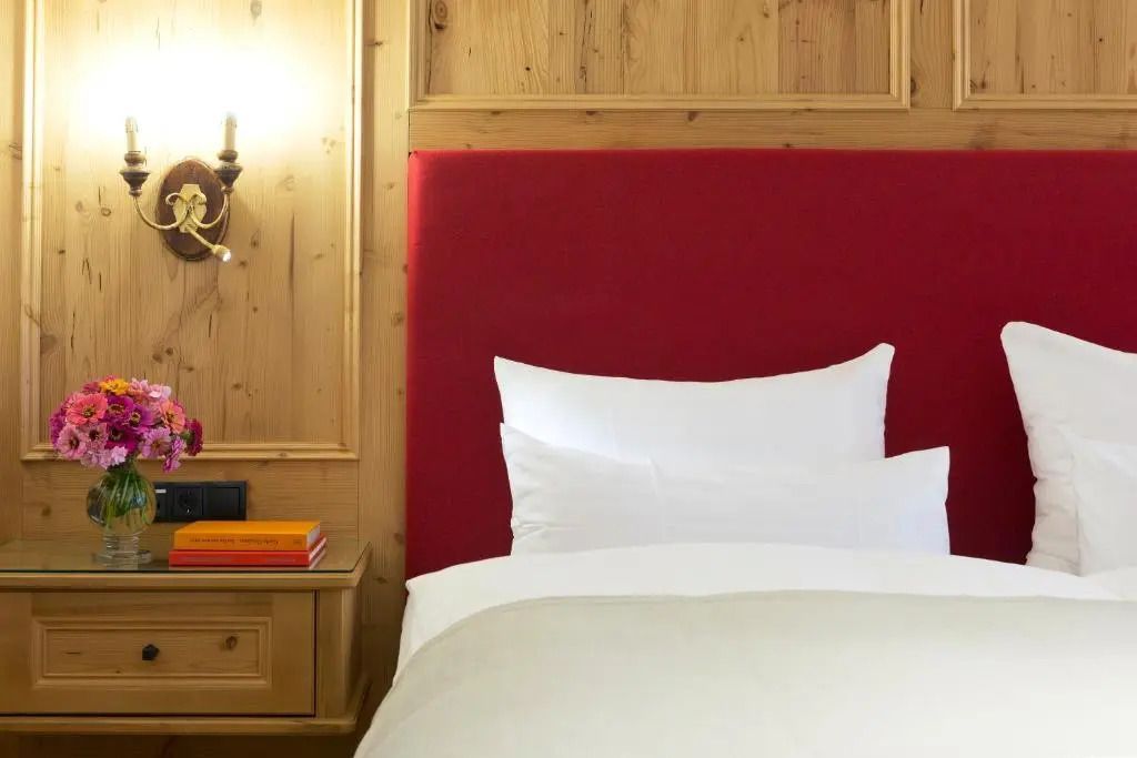 Einladendes Bett mit rotem Kopfteil und wandmontierter Lampe im Deluxe Zimmer.