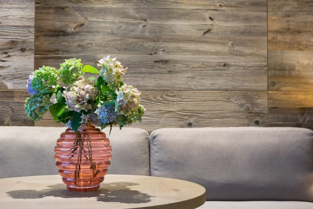 Runder Tisch mit Blumen in der Vase vor einer Holzvertäfelung im Wohnbereich