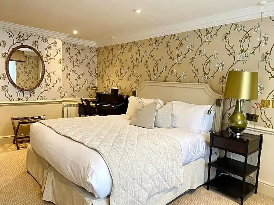 Klassisches Hotelzimmer mit floral gemusterter Tapete, Doppelbett und Schreibbereich