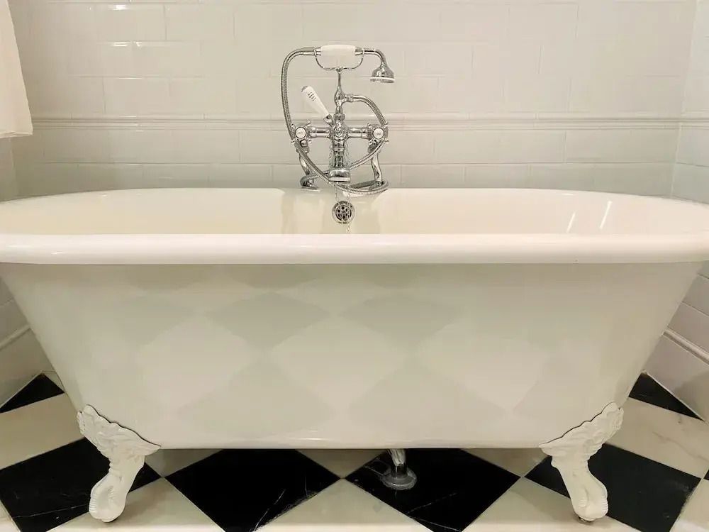 Freistehende weiße Badewanne mit nostalgischen Armaturen auf schwarz-weißem Fliesenboden