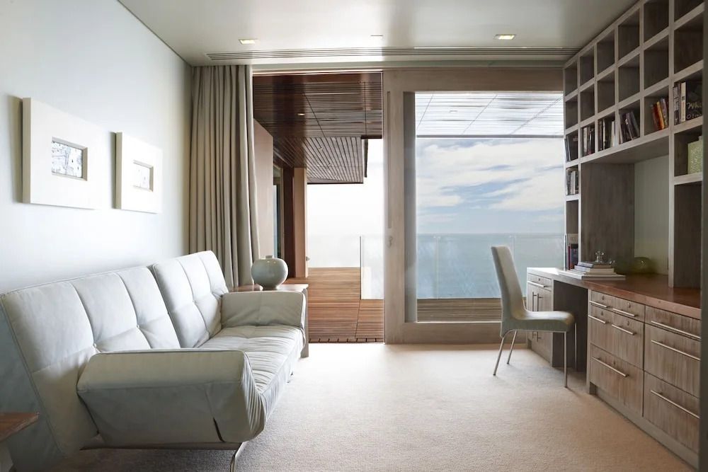 Helles Wohnzimmer mit Sofa und Schreibtisch, große Fenster mit Meerblick.