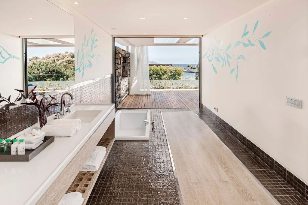 Hochwertiges Badezimmerdesign mit Natursteinfliesen und Terrasse mit Meerblick